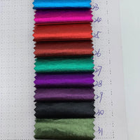 Une carte d'échantillons de Longan Craft France montre onze échantillons rectangulaires de Tissu lamé métallisé froissé au mètre de différentes couleurs, attachés verticalement sur une feuille avec des numéros écrits à la main à côté de chacun d'eux pour la couture créative et l'artisanat.