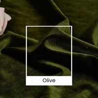 Gros plan sur le velours Tissu vert olive uni au mètre de Longan Craft France, aux plis souples et à la texture luxueuse. La mention "Olive" apparaît sur un carré blanc, mettant en valeur ce velours d'ameublement de 165 cm de large pour des projets créatifs.