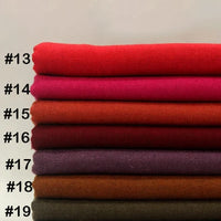 Une pile de tissu flanelle laine-polyester de Longon Craft France, étiquetée de #13 à #19, présente des teintes allant du rouge au marron foncé, idéales pour les vêtements d'hiver d'automne, pliées sur un fond neutre.